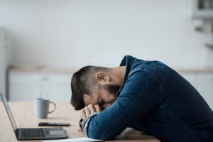 man resting head on desk, clearly distressed - compliance mistakes small businesses make