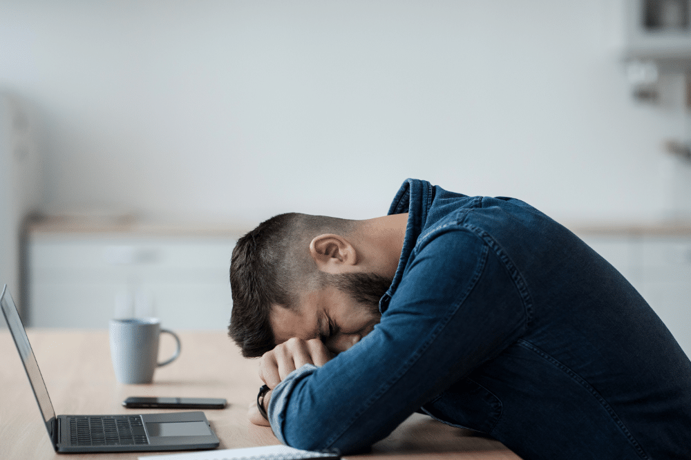 man resting head on desk, clearly distressed - compliance mistakes small businesses make